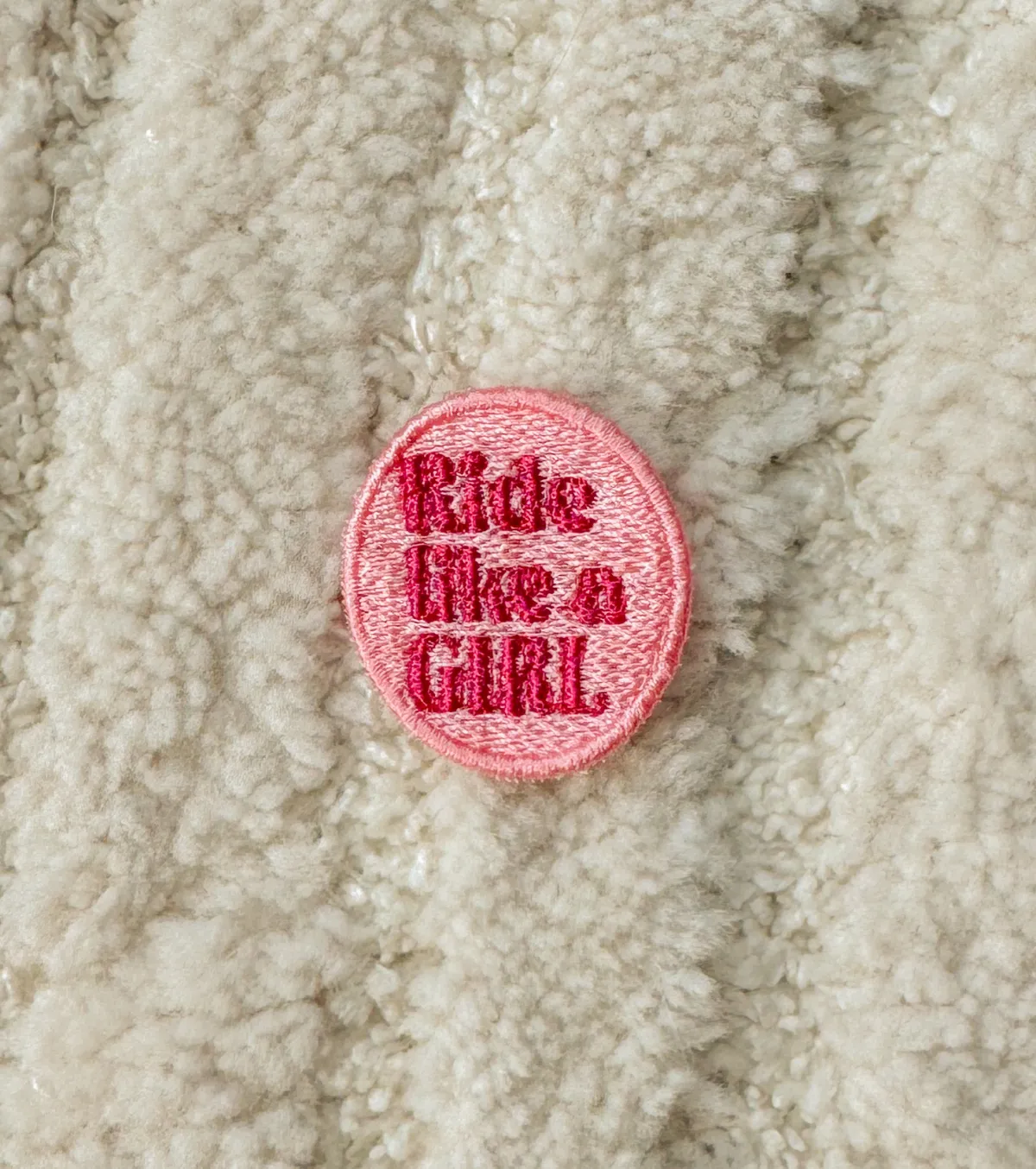 Pink oval Ride like a Girl embroidered patch on a cream sherpa jacket