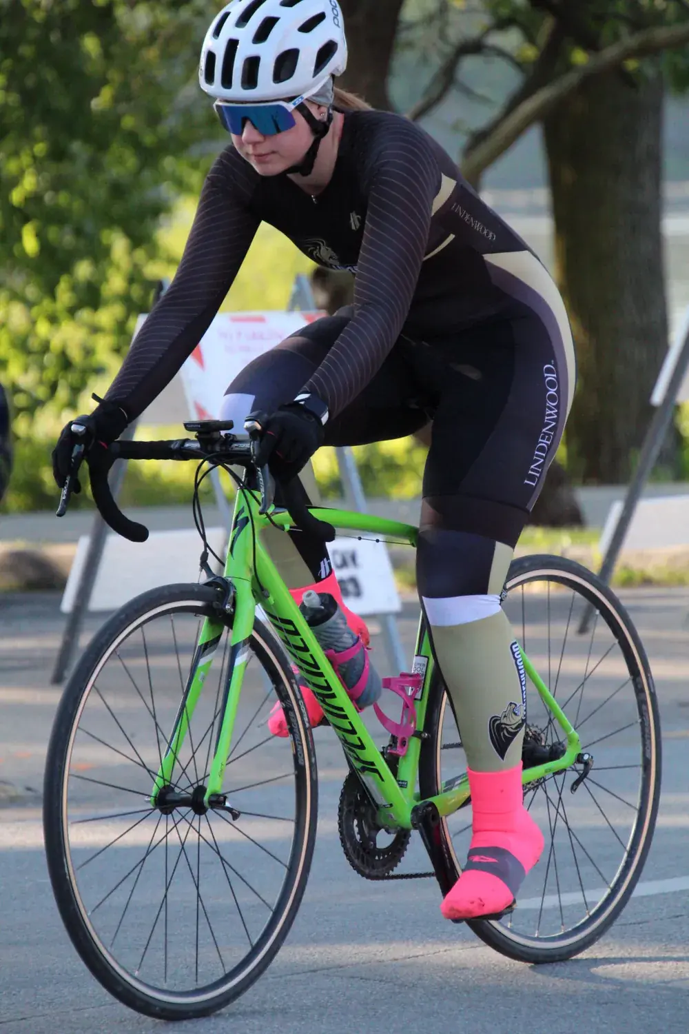 Addison riding her bright green road bike in her long-sleeve Lindenwood race kit, with neon pink socks