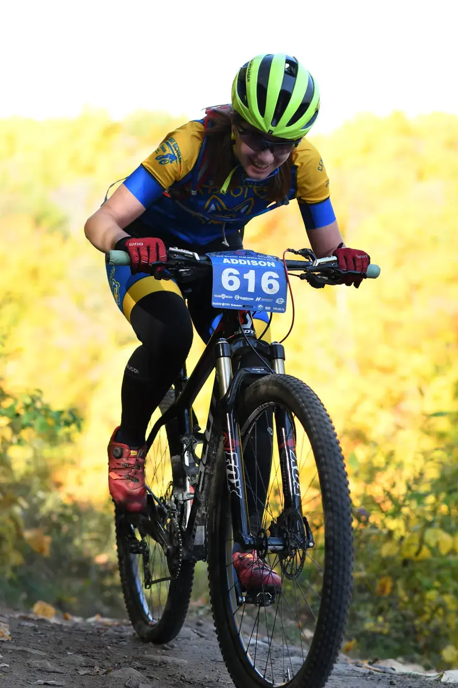 Addison racing a mountain bike up a leaf-covered trail, wearing race number 616